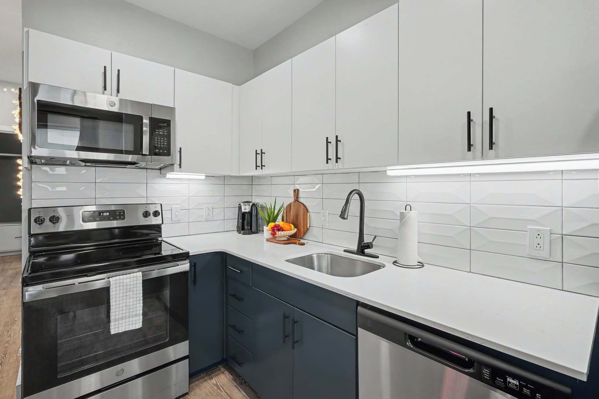 A modern kitchen with stainless steel appliances, white cabinetry, and a black dishwasher.