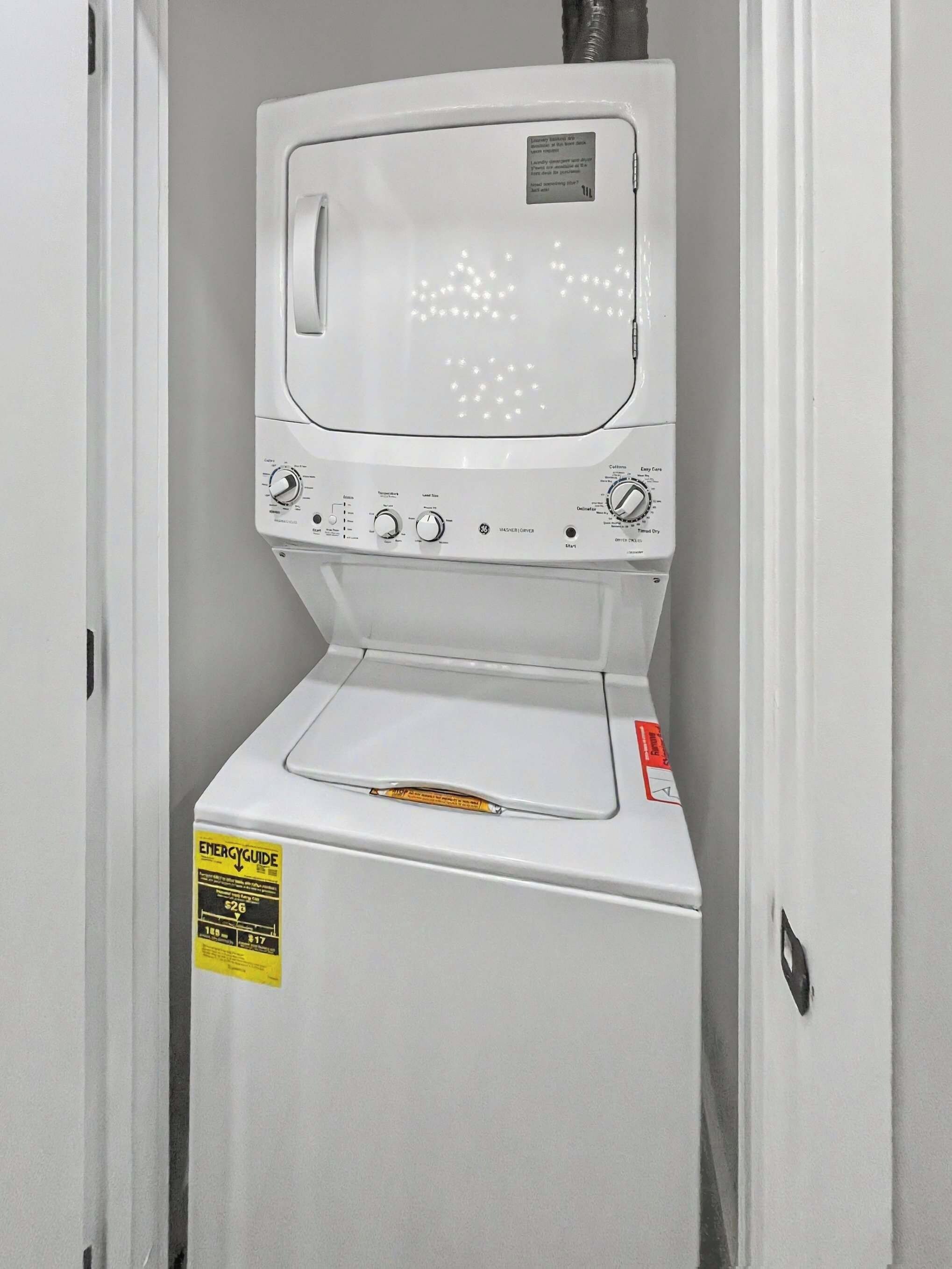 A front-loading white washer and dryer unit with an ENERGYGUIDE sticker, control knobs, and a label on the top.