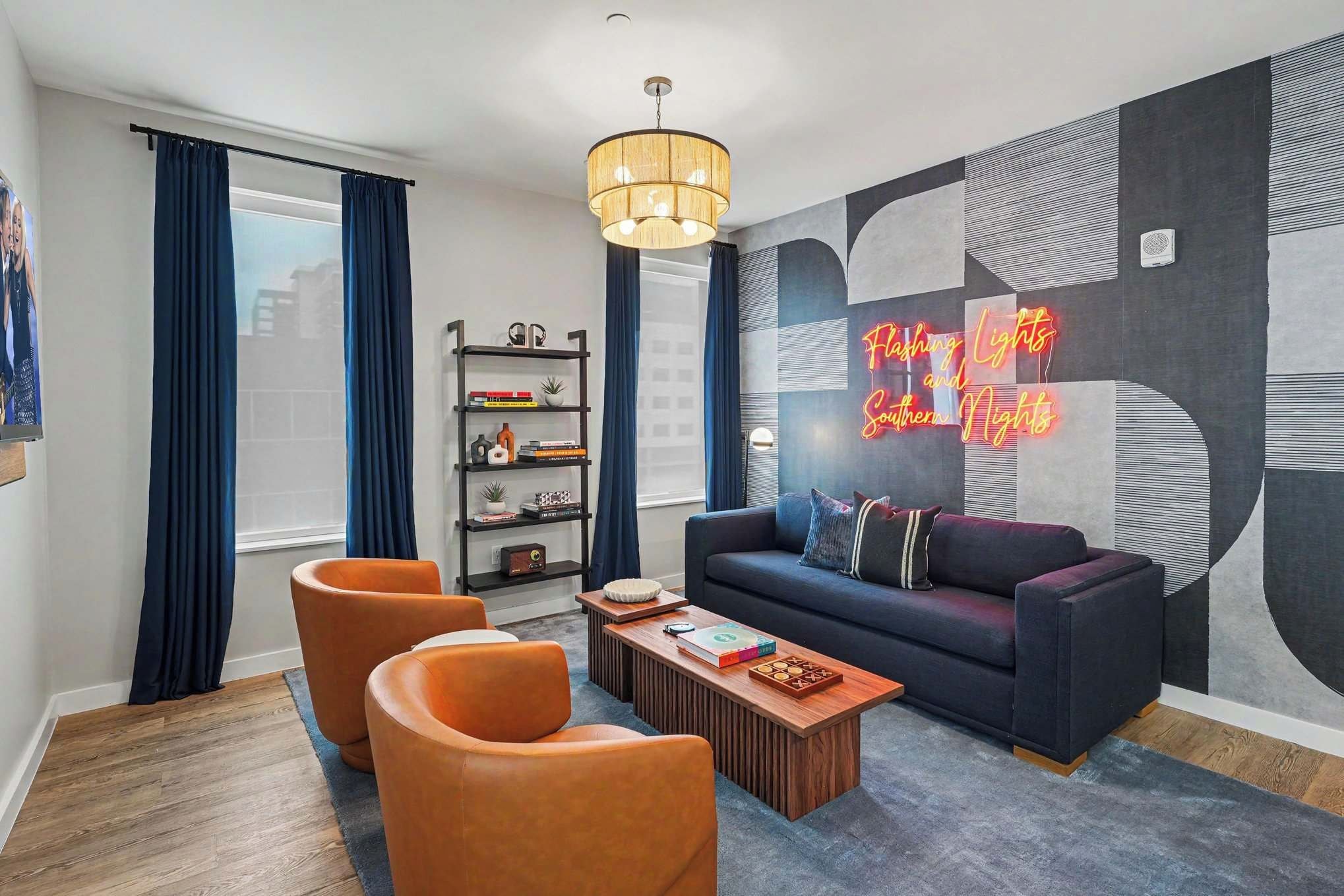 A modern living room with a sofa, two armchairs, a coffee table, a bookshelf, and a neon sign.