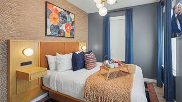 A modern bedroom with a wooden headboard, a bed with white bedding, a decorative wall art piece, a bedside table with a lamp, and a window with curtains.