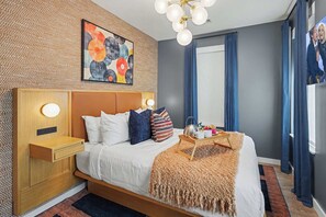 A modern bedroom with a wooden headboard, a bed with white bedding, a decorative wall art piece, a bedside table with a lamp, and a window with curtains. - Vinyl Retreat - Pool & Gym - Walk to Broadway (Nashville)