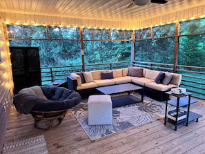 A covered outdoor seating area with a sectional sofa, a bean bag chair, and a small table with a projector.
