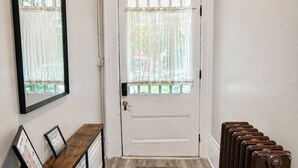 A hallway with a white door, a mirror, a wooden bench with framed pictures, and a radiator. - A Grand Historic Retreat-Downtown Covington-Sleeps 3 (Covington)