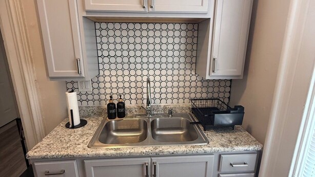 A compact kitchen with two sinks, a countertop with a paper towel holder, and a backsplash with hexagonal tiles. - A Grand Historic Retreat-Downtown Covington-Sleeps 3 (Covington)