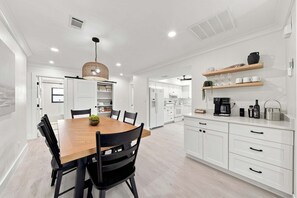 A modern kitchen with white cabinetry, a wooden dining table, and black chairs. - New! Blue Haven - Heated Saltwater Pool/Spa, 1 Mile to the Beach! (Naples)