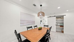 A dining area with a wooden table, black chairs, a pendant light, and a view into a room with a sliding door. - New! Blue Haven - Heated Saltwater Pool/Spa, 1 Mile to the Beach! (Naples)