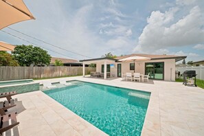Ein Garten mit Schwimmbad, Terrassenmöbeln und Grill.