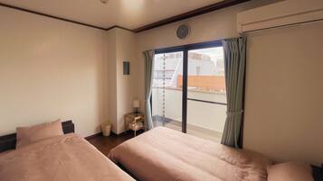 Een hotelkamer met twee bedden, een klein nachtkastje met een lamp, een raam met gordijnen en uitzicht op gebouwen.