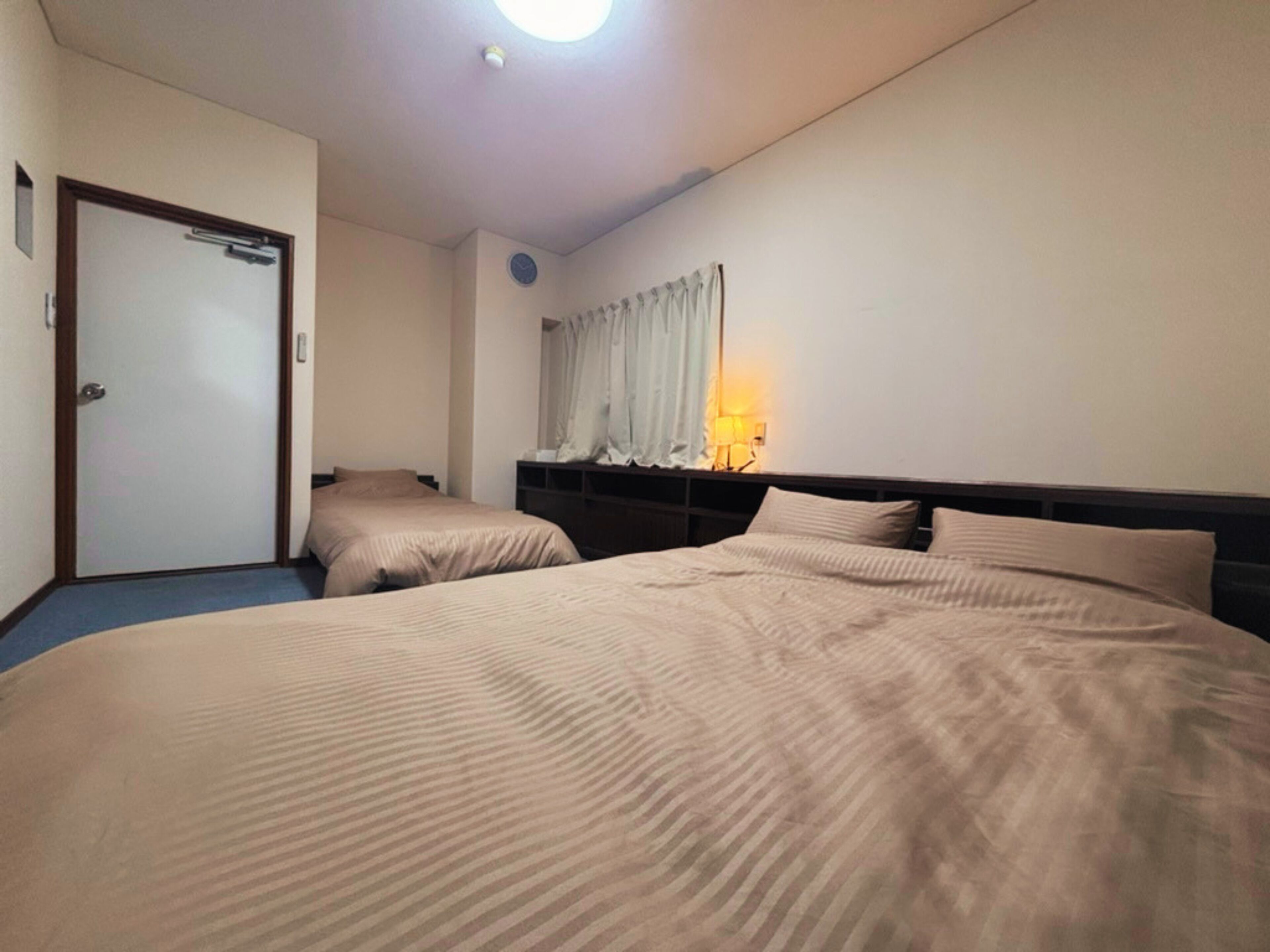 A hotel room with two beds, a door, a nightstand, and a wall-mounted lamp.