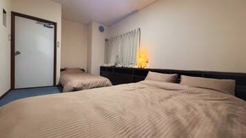 A hotel room with two beds, a door, a nightstand, and a wall-mounted lamp.