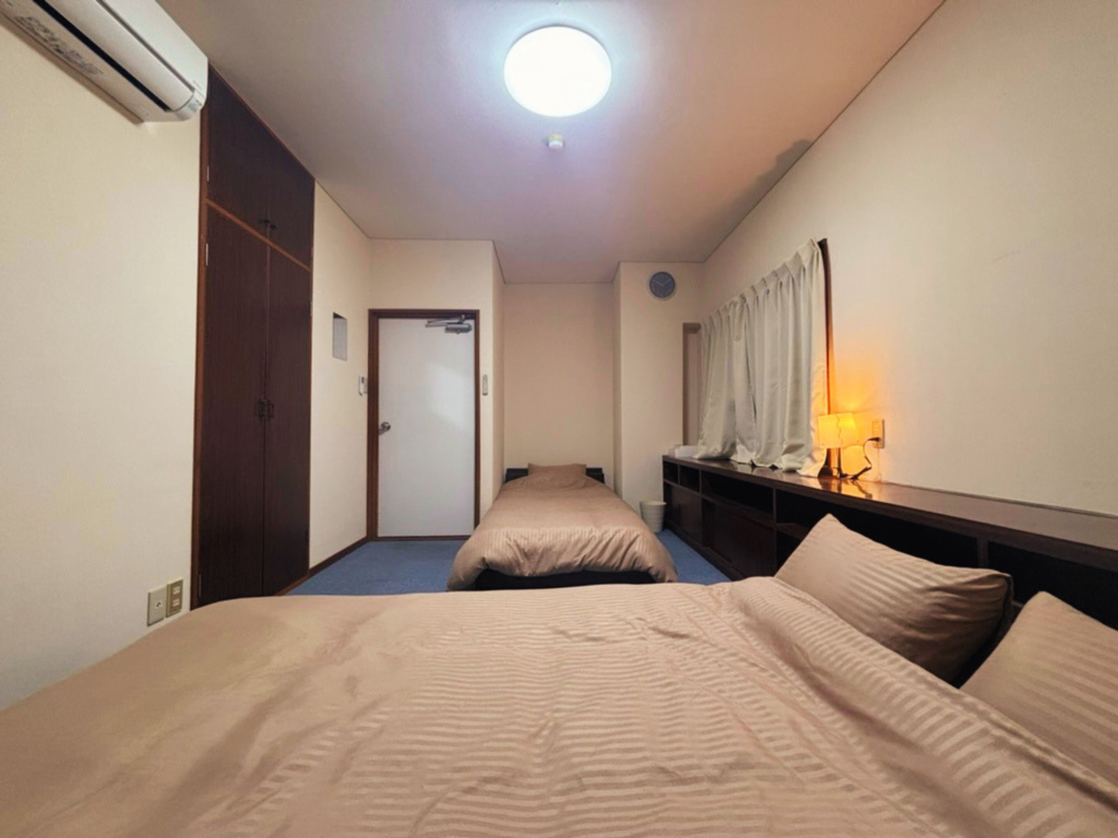 A hotel room with a bed, a desk, a lamp, a wardrobe, and a door.