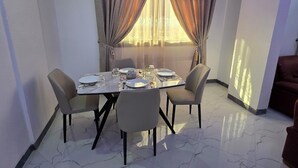 A dining area with a table set for four, chairs, and a window with curtains. - Appart hotel 3 bed room ADAMA SOW  (Dakar)