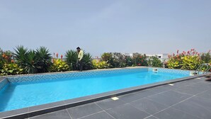 A rooftop swimming pool with a tiled edge, surrounded by lush greenery and flowering plants. - Appart hotel 3 bed room ADAMA SOW  (Dakar)