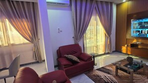 A modern living room with a red sofa, a glass coffee table, and a television on a wooden wall. - Appart hotel 3 bed room ADAMA SOW  (Dakar)