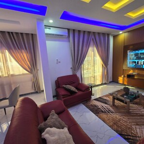 A modern living room with a red sofa, a glass coffee table, and a television on a wooden wall.
