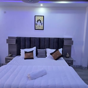 A neatly made bed with pillows and a folded towel, a wall-mounted artwork, and bedside lamps. - Appart hotel 3 bed room ADAMA SOW  (Dakar)
