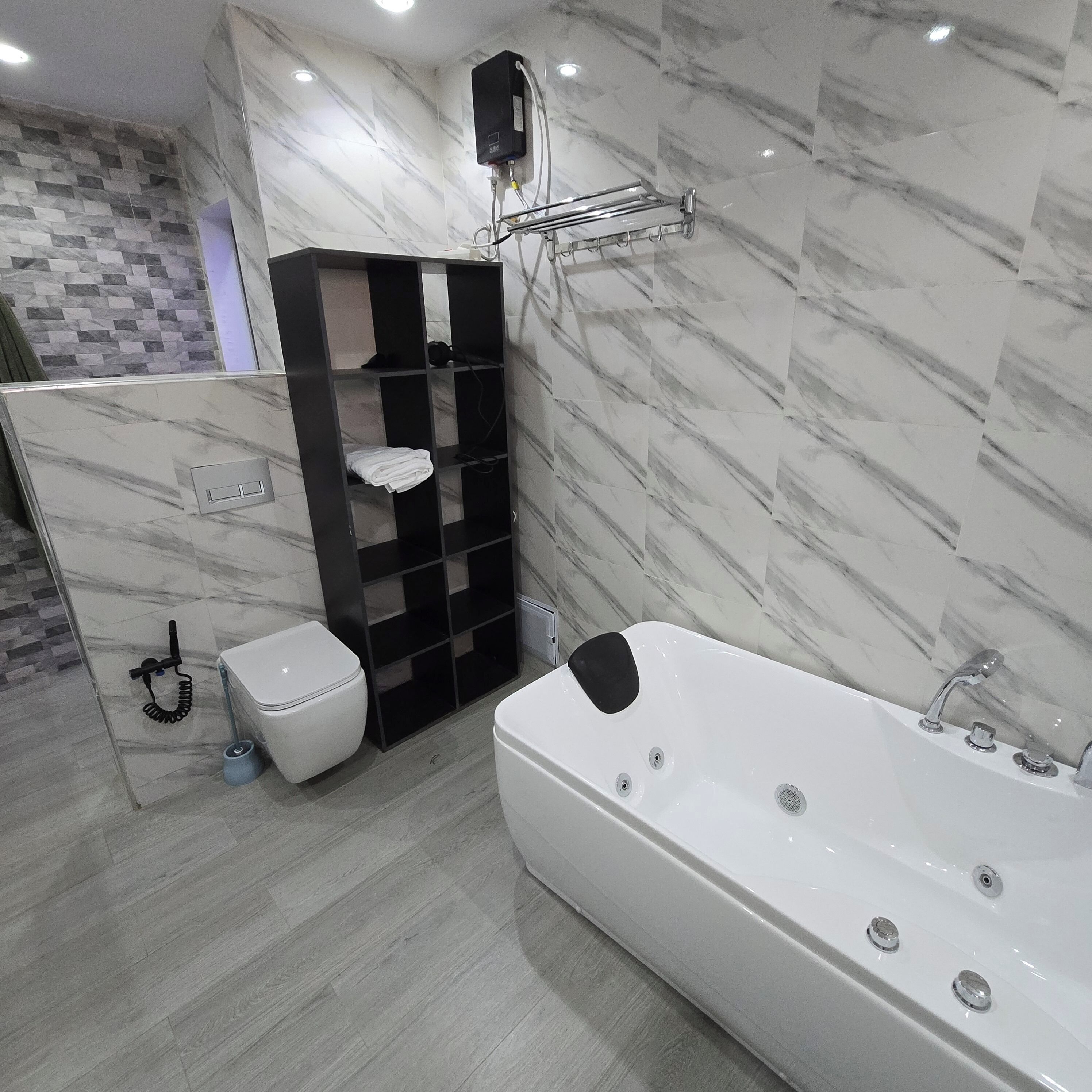 A modern bathroom with a white bathtub, a black shelf unit, a toilet, and a shower area.