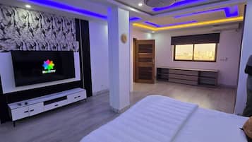 Une chambre à coucher avec un lit, une télévision, un ventilateur de plafond et une fenêtre donnant sur la ville.