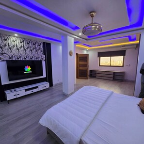Un dormitorio con cama, televisor, ventilador de techo y ventana con vista a la ciudad.