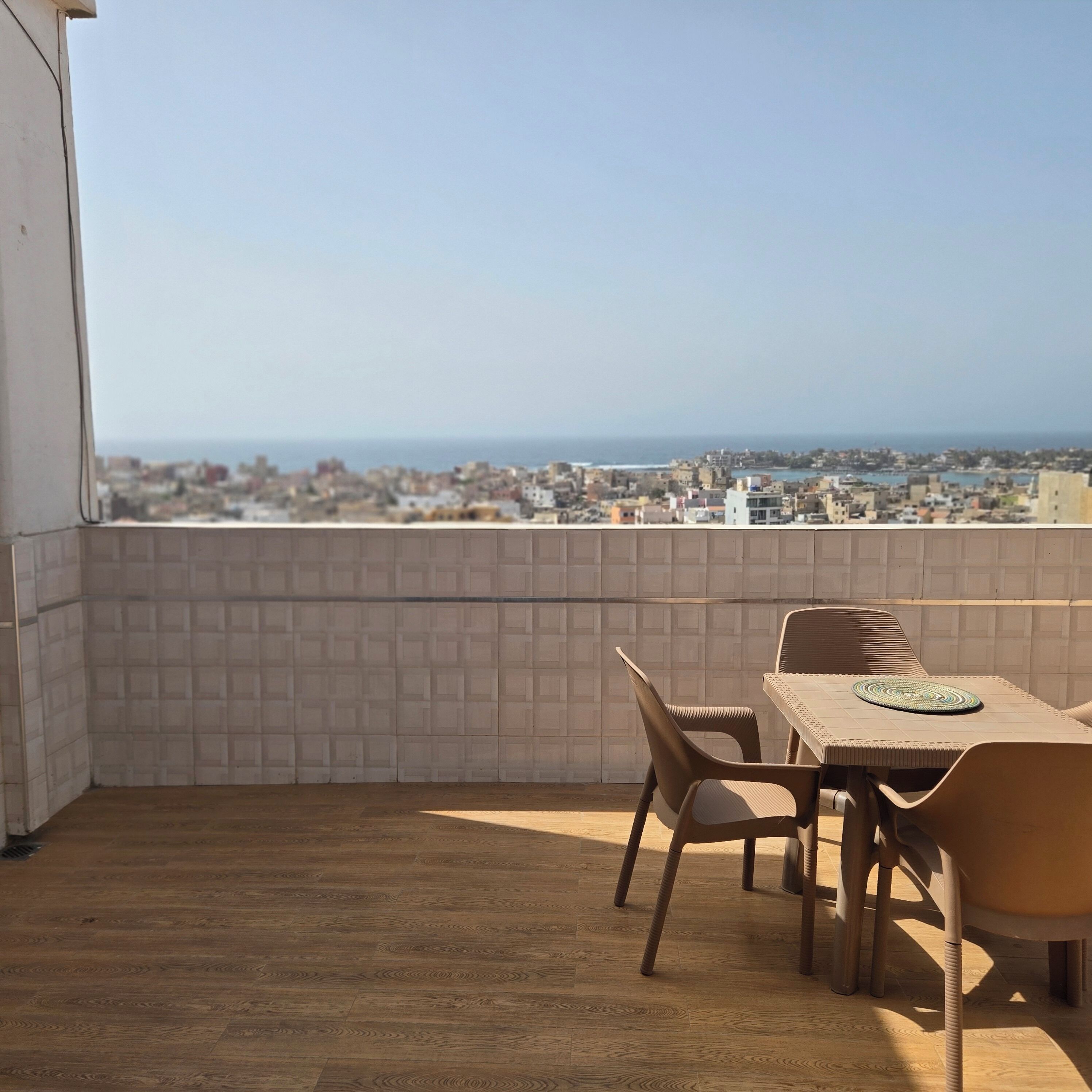 Un balcón con suelo de madera, una mesa con sillas y vistas a la ciudad y al mar.