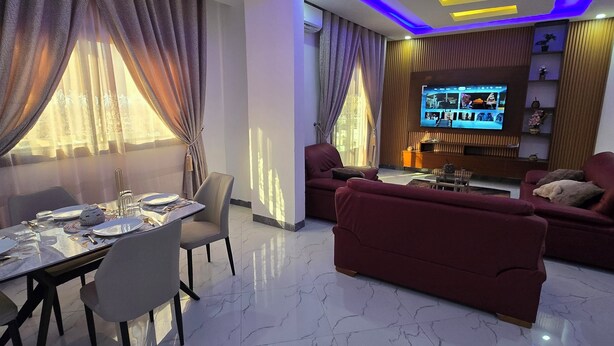A modern living room with a dining area, a flat-screen TV, and a sofa. - Appart hotel 3 bed room ADAMA SOW  (Dakar)