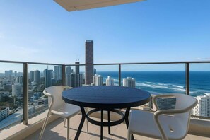 Ein Balkon mit rundem Tisch und zwei Stühlen, Blick auf Stadt und Meer.