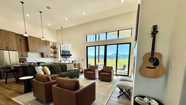 A spacious living room with a large window, a dining area, and a kitchen. - RollingTetonRetreat_Hot tub_Sauna_Patio_FamilyFriendly (Tetonia)
