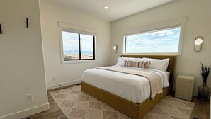 A bedroom with a large bed, two windows, a nightstand, and a wall-mounted lamp. - RollingTetonRetreat_Hot tub_Sauna_Patio_FamilyFriendly (Tetonia)