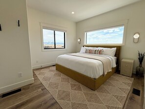 Ein Schlafzimmer mit einem großen Bett, zwei Fenstern, einem Nachttisch und einer Wandlampe.
