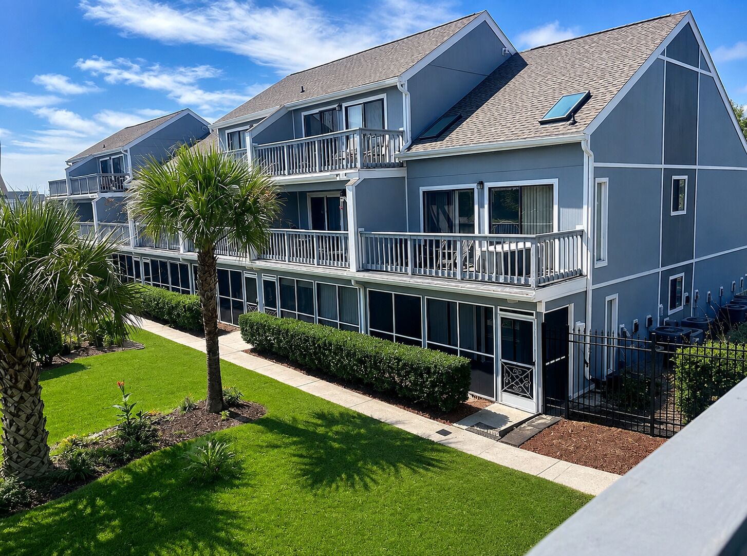 A multi-story residential building with balconies, a covered outdoor area, and a well-maintained lawn.