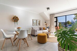 Ein modernes Wohnzimmer mit Essbereich, einer Couch, einem Couchtisch und einem großen Fenster mit Blick nach draußen.