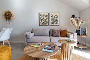 A modern living room with a grey sofa, two side tables, a coffee table, and a bookshelf with plants. - Stylish one bedroom apartment in quiet estate near the vineyards (Cape Town)