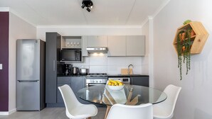 Moderni keittiö, jossa on lasinen ruokapöytä, valkoiset tuolit ja hedelmäkulho.