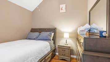 A bedroom with a bed, bedside table, lamp, dresser, and a framed picture on the wall.