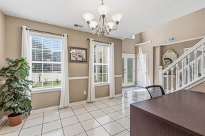 A spacious room with large windows, a chandelier, a staircase, and a potted plant. - 5BR/3BA Retreat | Near Stone Mountain | Sleeps 10 (DeKalb County)