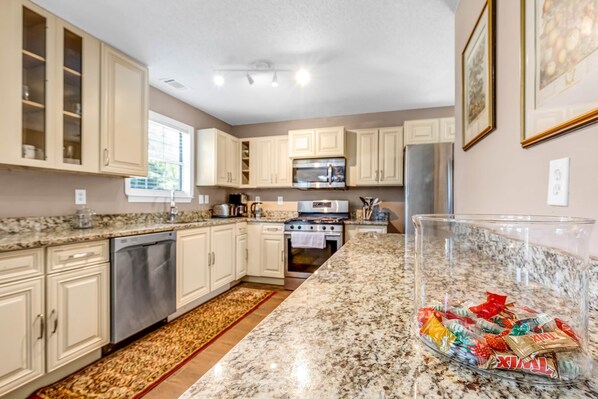 A modern kitchen with granite countertops, stainless steel appliances, and light-colored cabinetry. - 5BR/3BA Retreat | Near Stone Mountain | Sleeps 10 (DeKalb County)