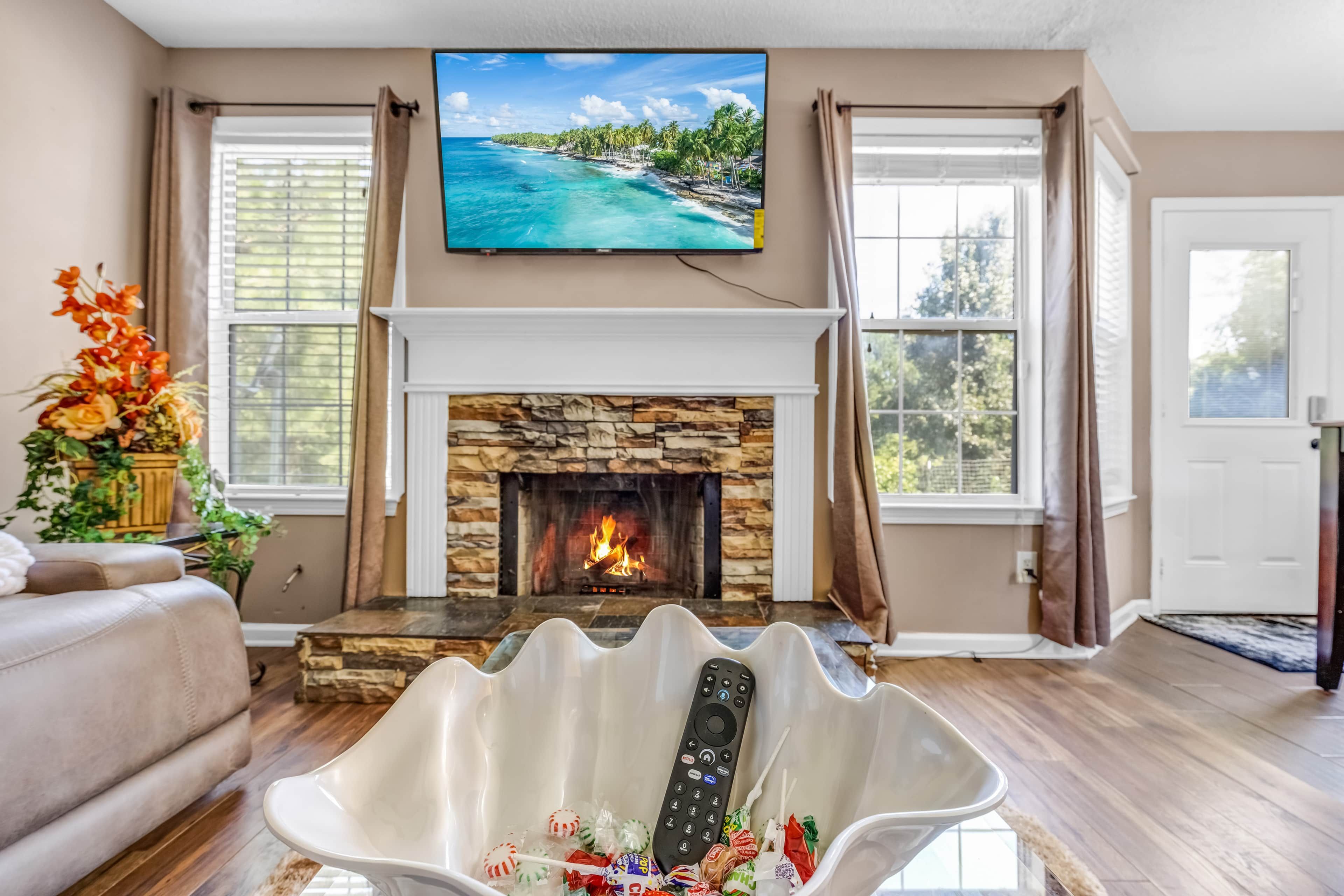 A living room with a fireplace, a television mounted above it, and a remote control on a white stand.
