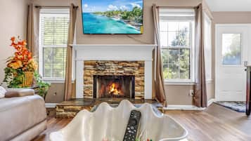 A living room with a fireplace, a television mounted above it, and a remote control on a white stand.