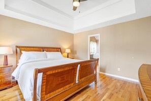 A bedroom with a wooden bed, bedside tables, a ceiling fan, and a view of the bathroom. - 5BR/3BA Retreat | Near Stone Mountain | Sleeps 10 (DeKalb County)