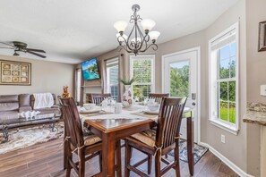 A dining area with a table set for four, a ceiling fan, and a TV mounted on the wall. - 5BR/3BA Retreat | Near Stone Mountain | Sleeps 10 (DeKalb County)