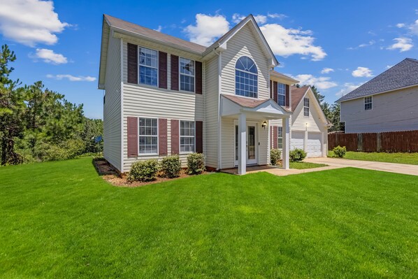 A two-story house with a front porch, a garage, and a well-maintained lawn. - 5BR/3BA Retreat | Near Stone Mountain | Sleeps 10 (DeKalb County)
