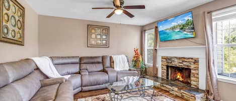 A living room with a sectional sofa, a fireplace, a ceiling fan, and a television on the wall.