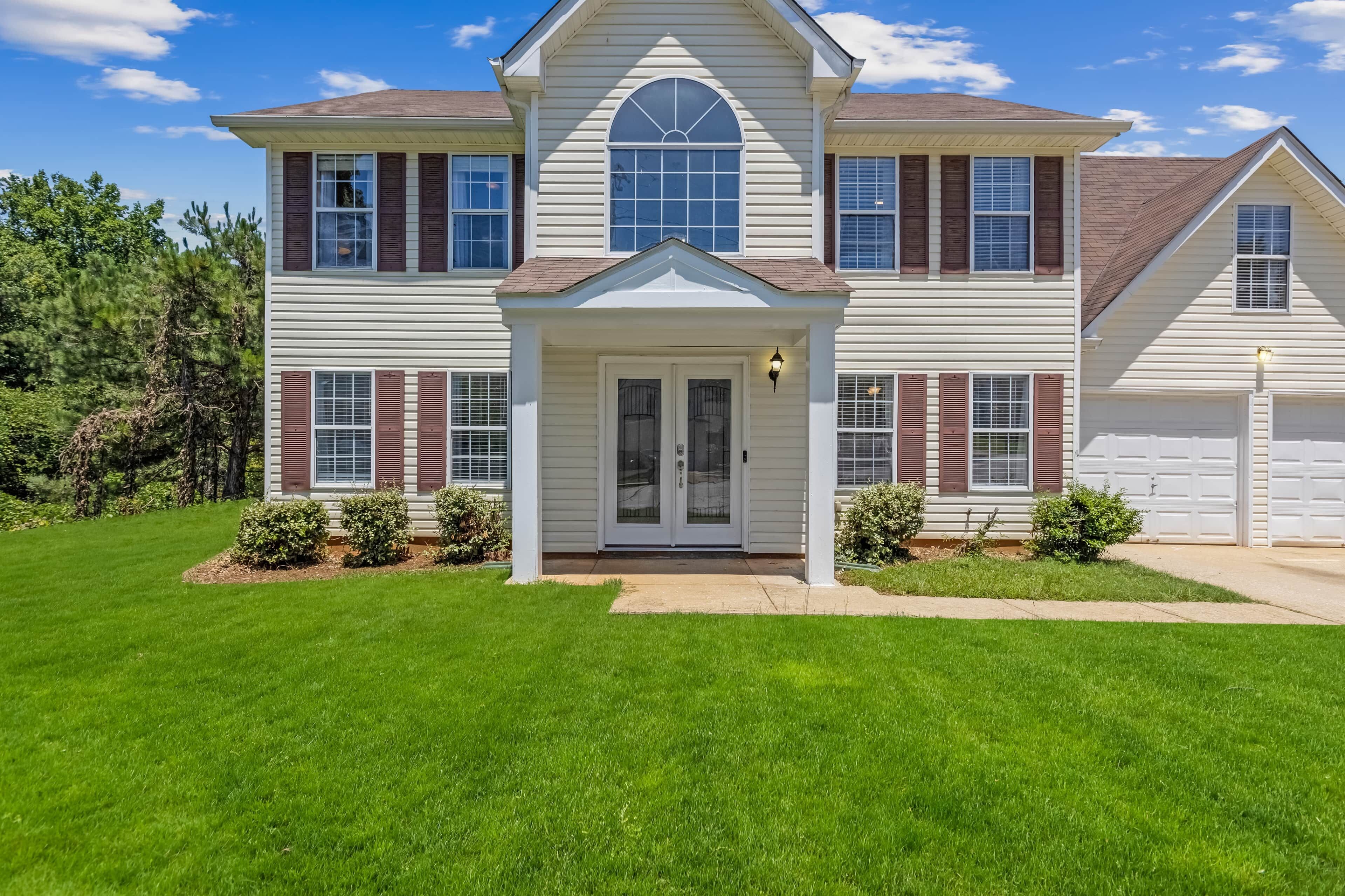 A two-story house with a front porch, a garage, and a well-maintained lawn.