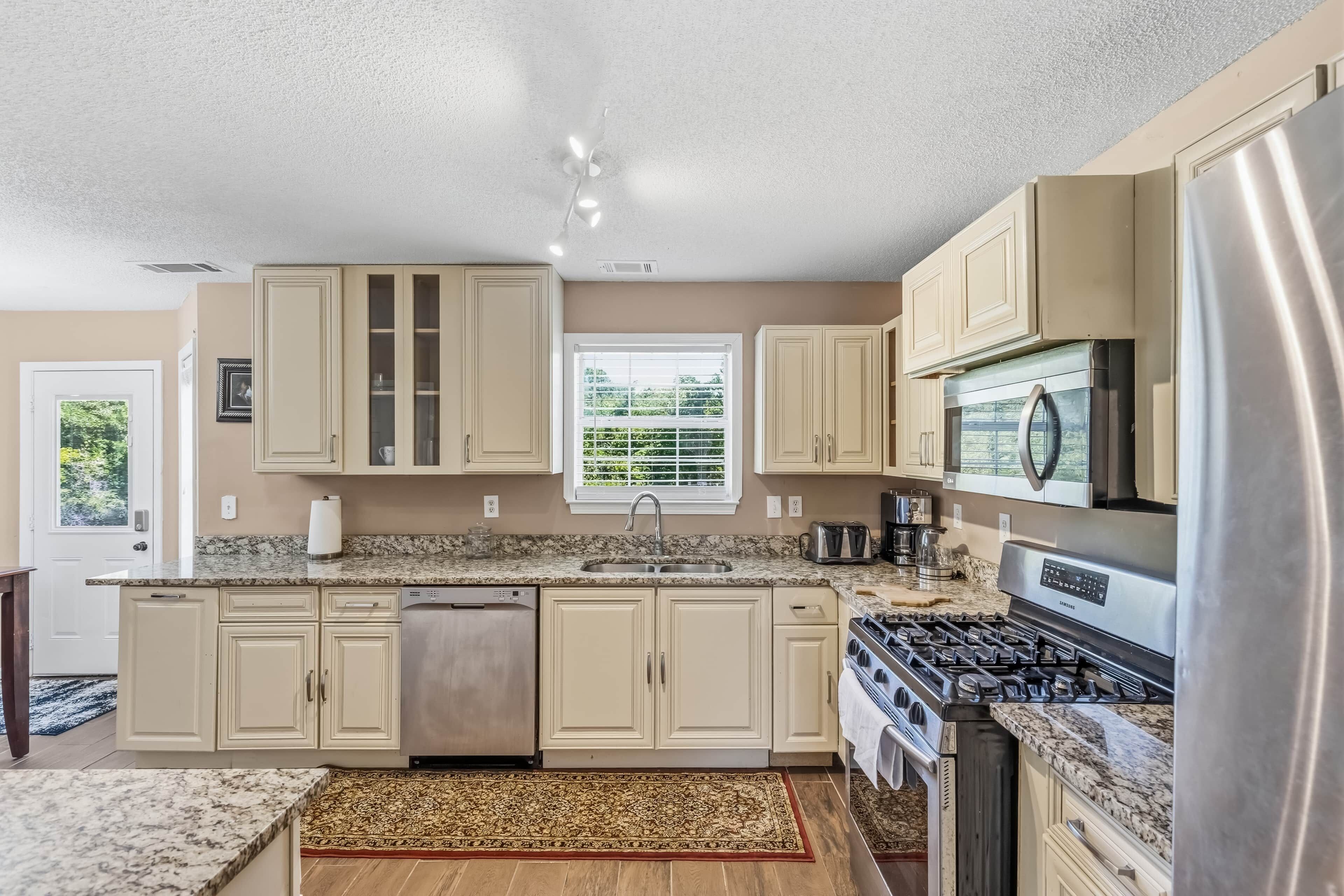 A modern kitchen with beige cabinetry, a stainless steel refrigerator, a built-in oven, and a granite countertop.