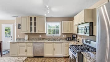 A modern kitchen with beige cabinetry, a stainless steel refrigerator, a built-in oven, and a granite countertop.