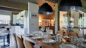 Un coin repas avec une table en bois dressée pour le repas, entourée de chaises, et un grand luminaire suspendu au-dessus.