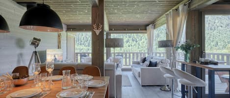 A dining area with a wooden table set for four, surrounded by chairs, and a sofa with cushions.