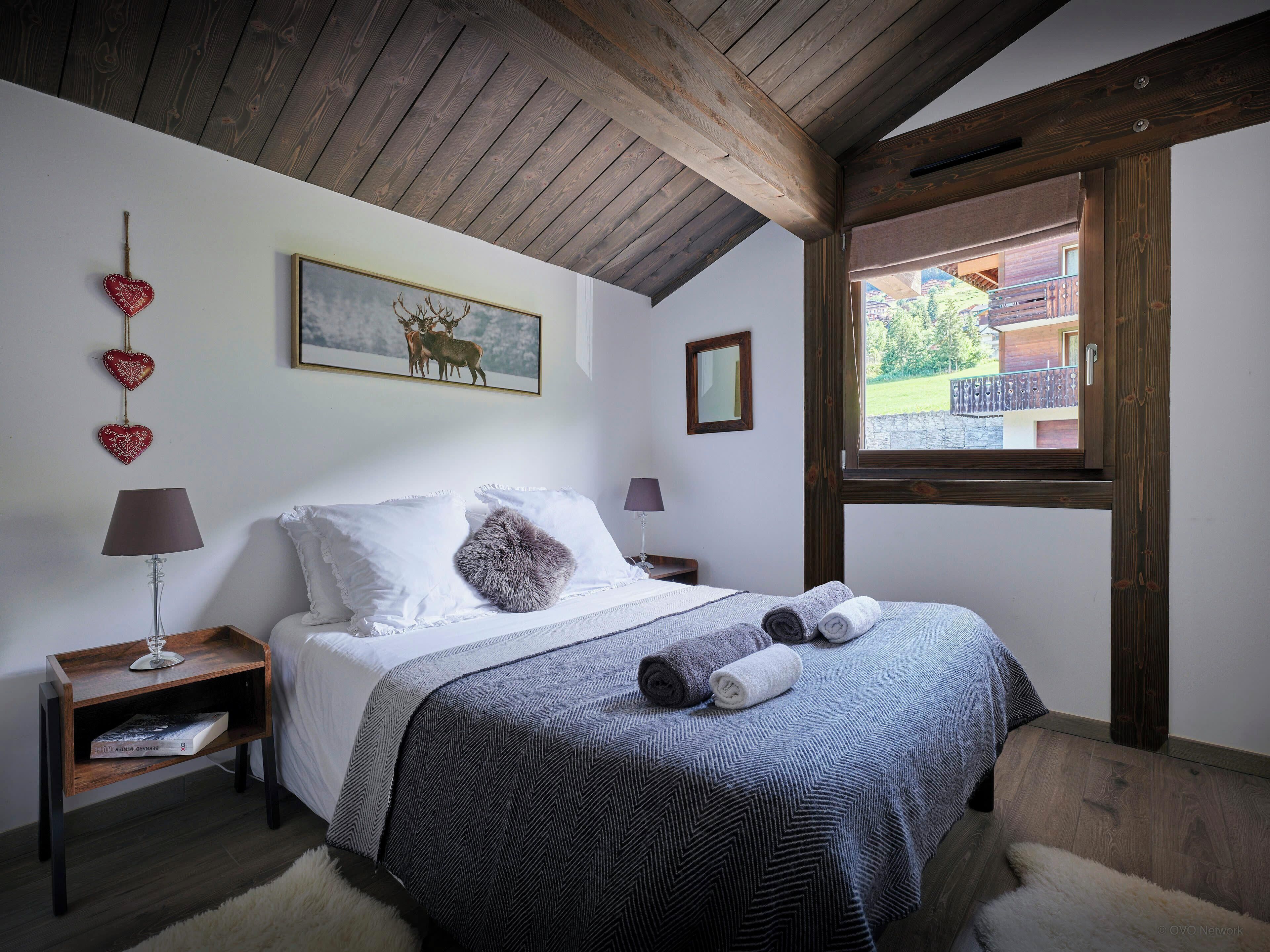 A bedroom with a bed, two bedside tables, a window, and a painting on the wall.