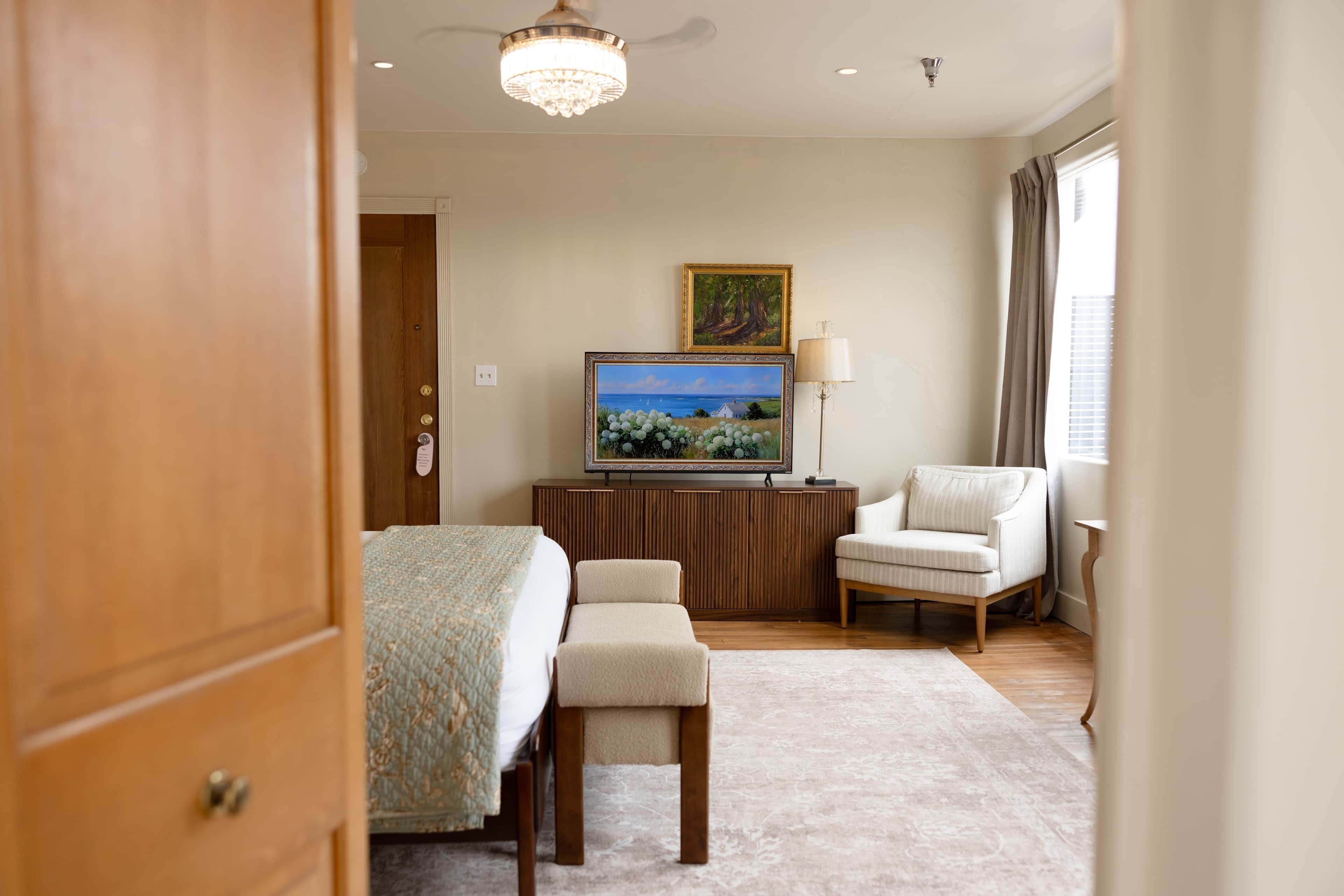 A hotel room with a bed, a desk, a chair, a television, and a window with curtains.