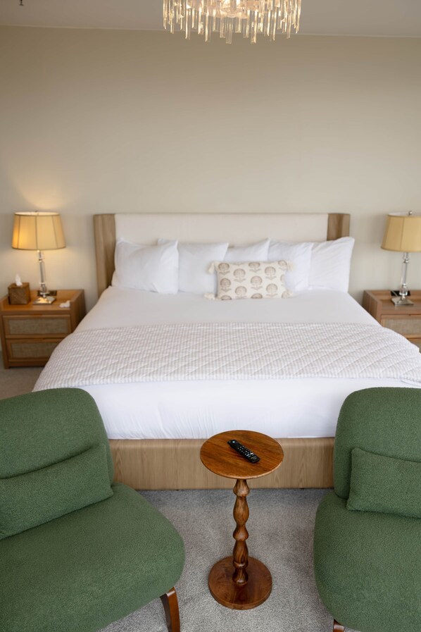 Habitació d'hotel amb un llit, dues làmpades de nit, una taula de fusta petita amb un comandament a distància i dues butaques verdes.